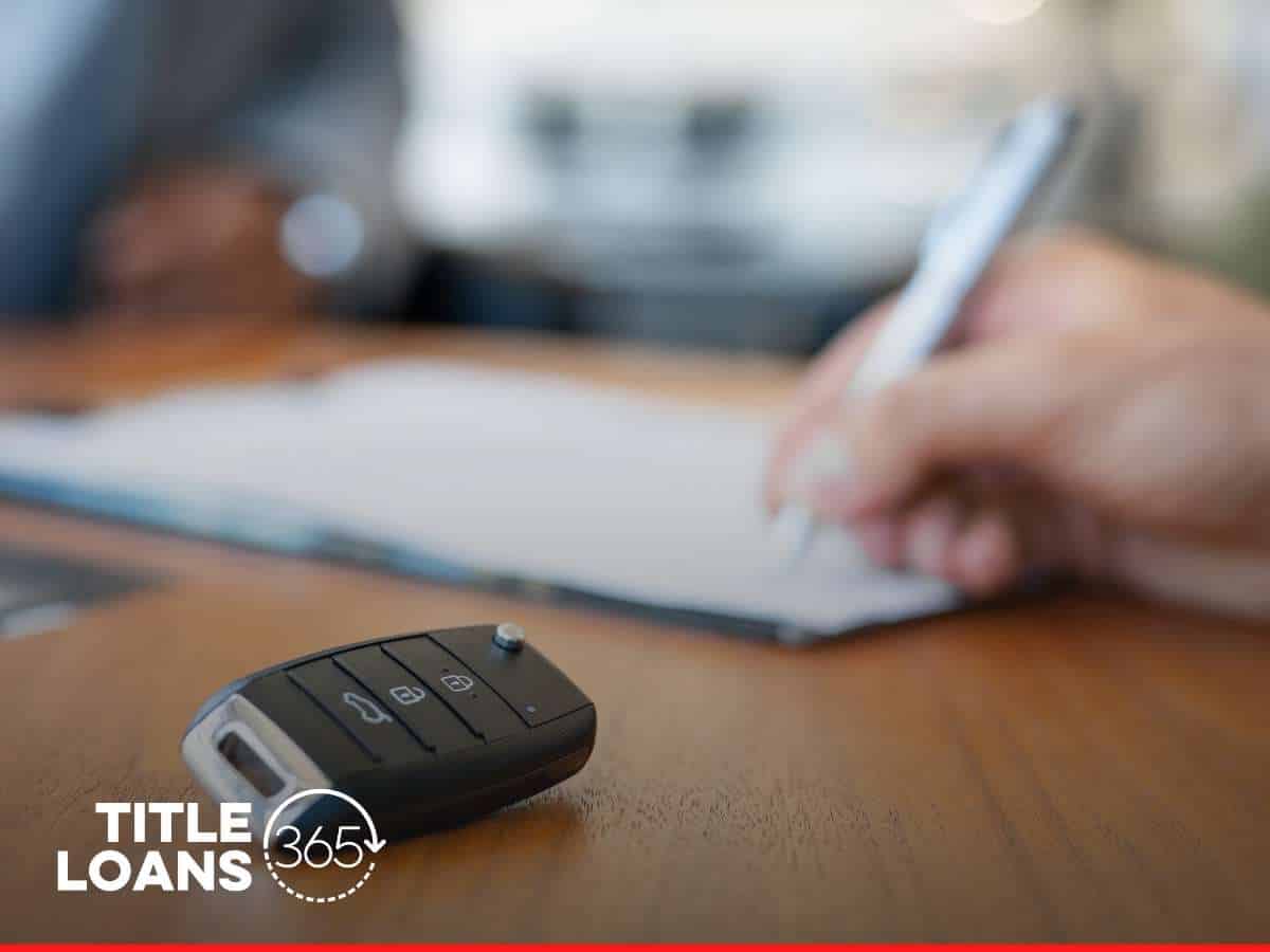 Close-up of a person's hand signing a document for a Truck Title Loan, with car keys in the foreground and Title Loans 365 logo